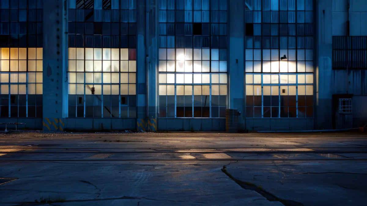 A row of old factory windows glowing amber in the evening light, brick wall beyond.