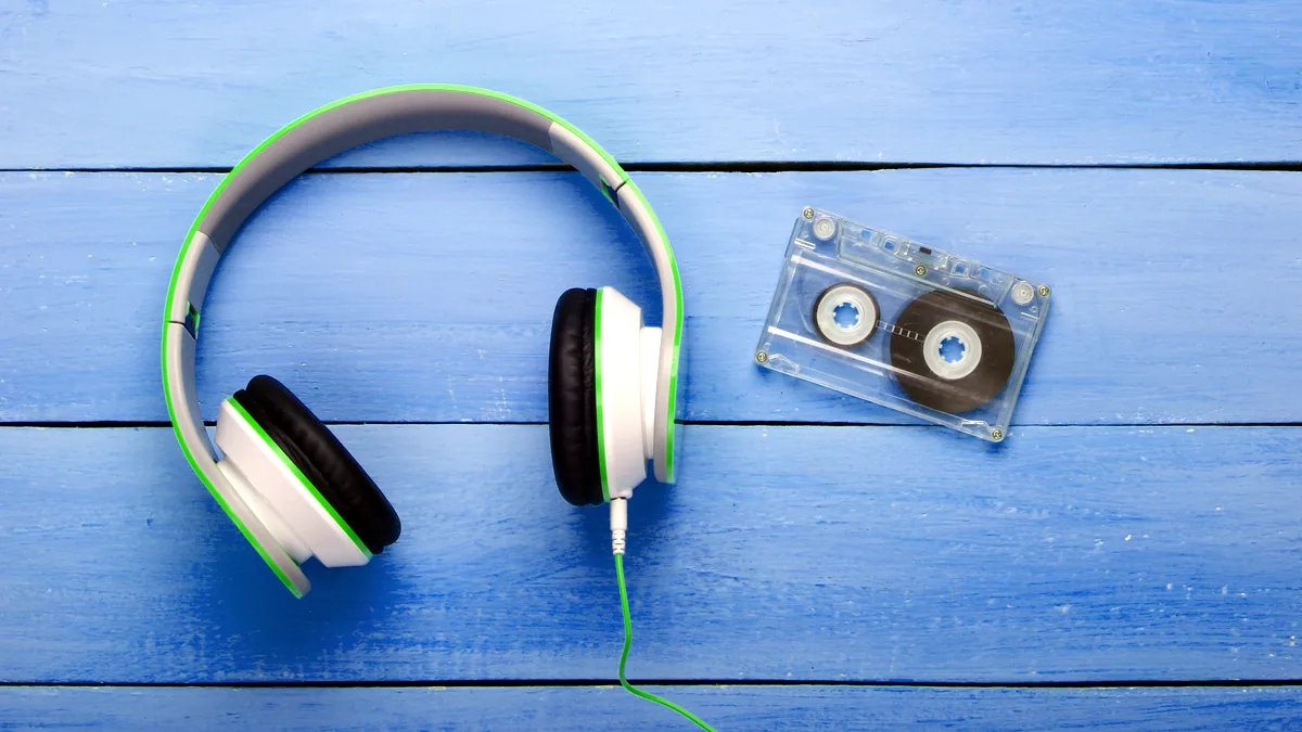 A pair of headphones and a cassette tape on a desk, the cable loosely coiled.