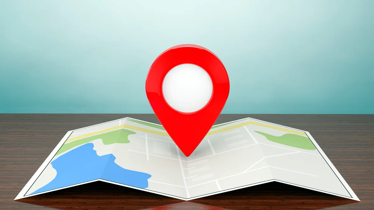 A folded paper city map spread on a table, a finger holding down a street name.