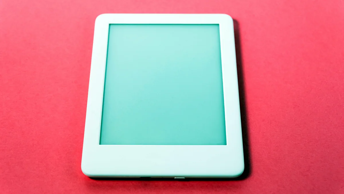 A small white e-reader tablet with a glowing screen, resting on an open newspaper.