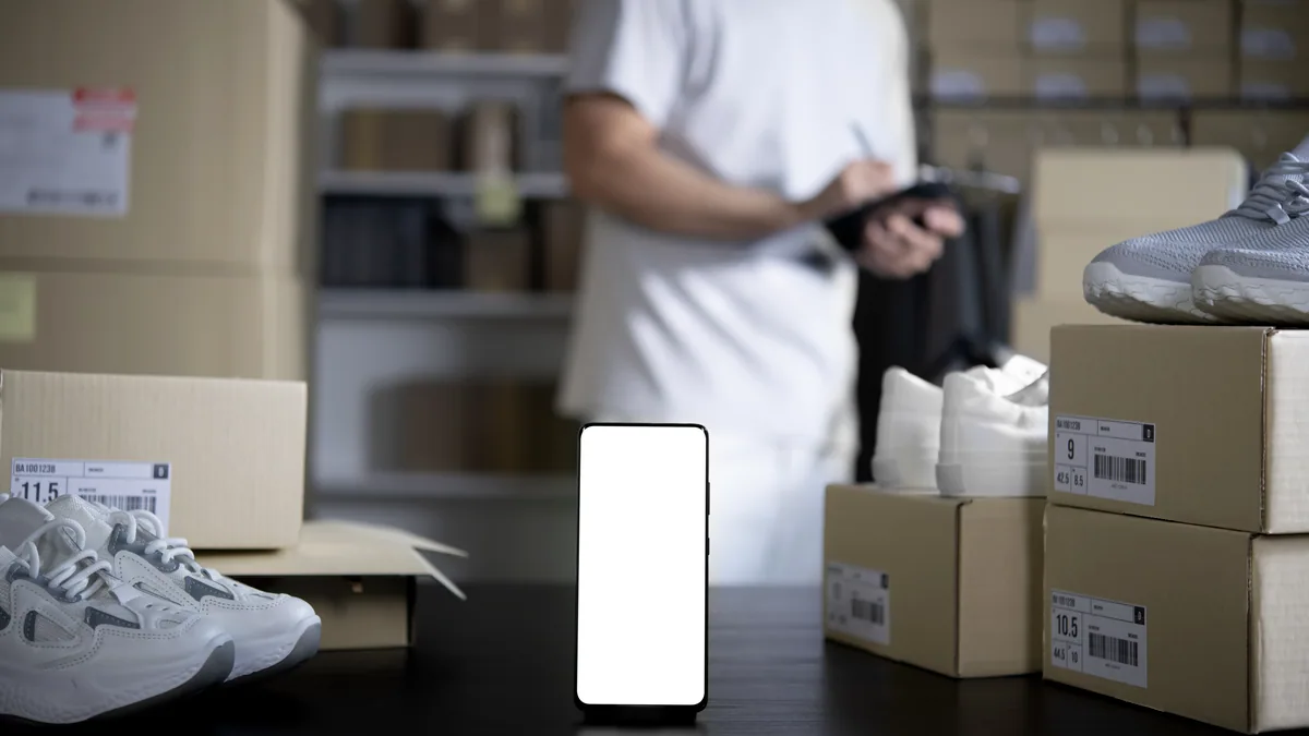 A slim smartphone standing upright in an open cardboard box, packing foam pushed to one side.