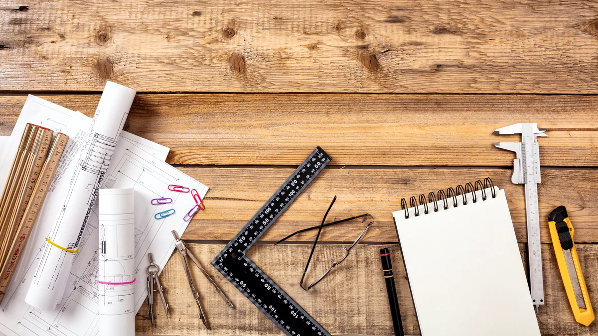 A blue blueprint held flat on a drafting table, a metal ruler laid across a corner.